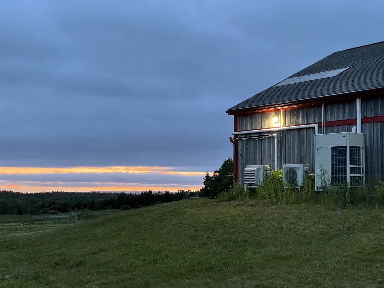 A vast sunset on an open valley, one barn stands in the field with a single light on 